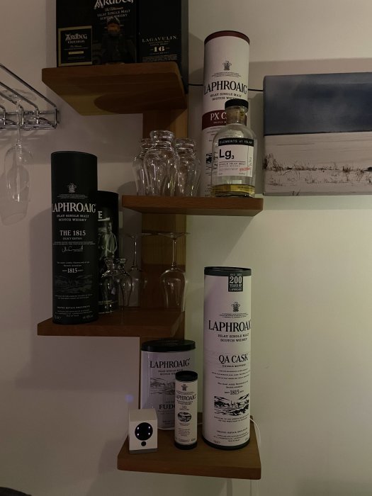 En samling whiskyer och glas på trähyllor, med en Laphroaig-tema och inramade bilder.