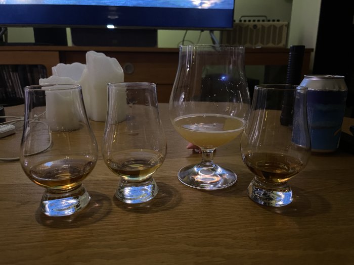 Fyra whiskeyglas, ett ölglas, en ölburk, och en tänd ljusstake på ett bord.