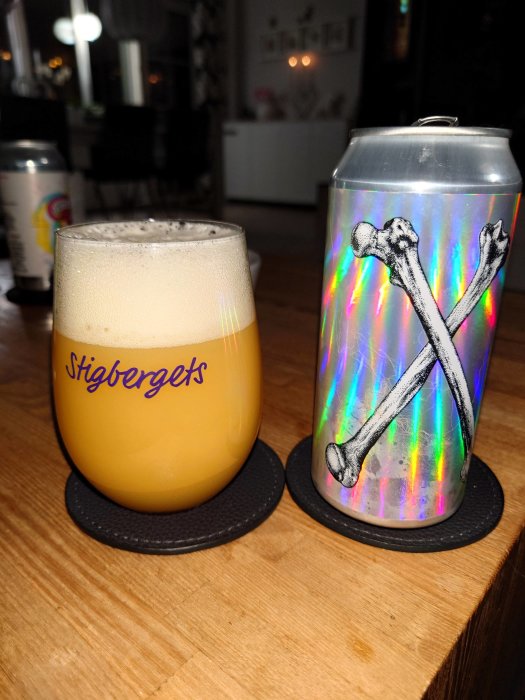 Ett glas öl och en burk med holografisk design på ett träbord. Coasters. Inomhusmiljö.