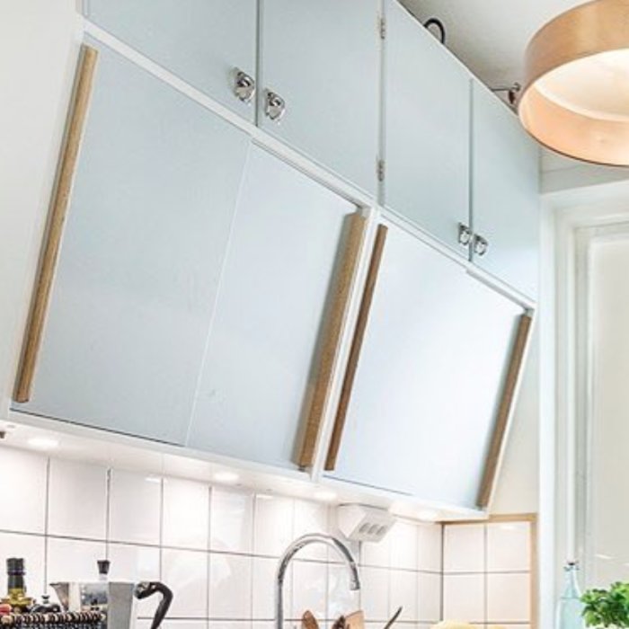 Blå köksskåp med trähandtag, vita kakelplattor, diskbänk och en modern, rund taklampa.