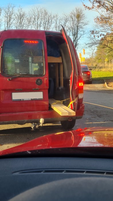 Röd skåpbil med öppen bakdörr transportera möbel säkrad med spännband, dagtid, bilkö.