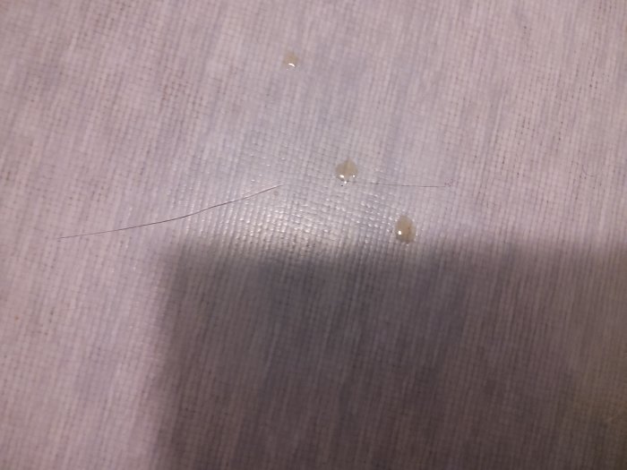 Enstaka hårstrå och små droppar på en strukturerad yta med skugga. Otydligt, vardagligt, närbild.