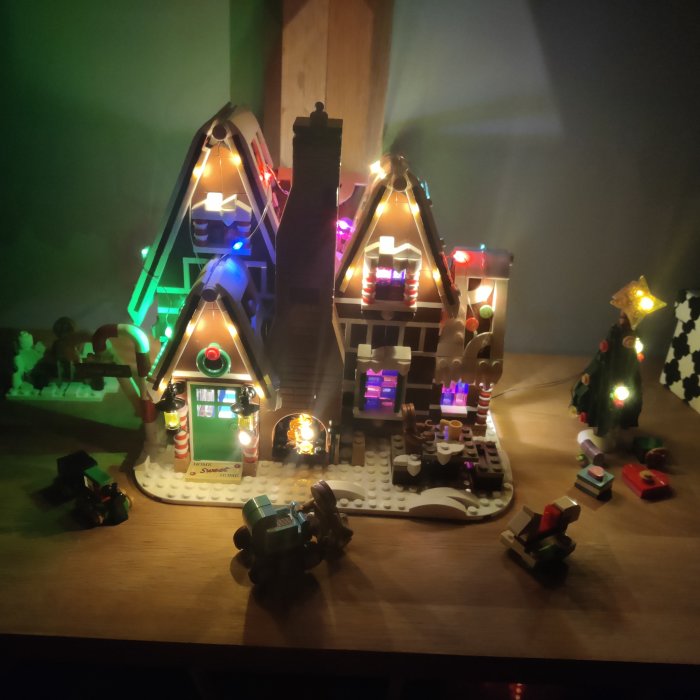 Modell av ett juldekorerat hus med ljus, gran och figurer, troligen av LEGO eller liknande byggklossar.