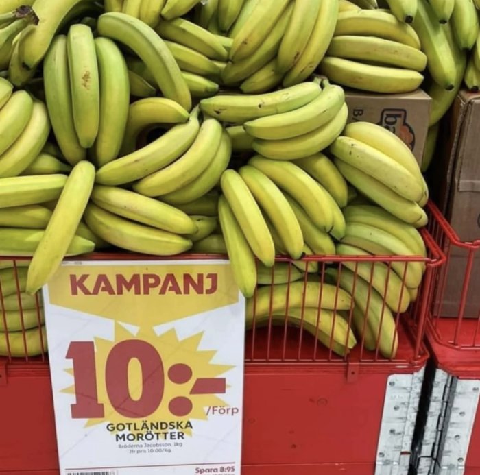 Bananhög i en röd korg med felmärkt kampanjskylt för 'Gotländska morötter' istället. En humoristisk misstag.