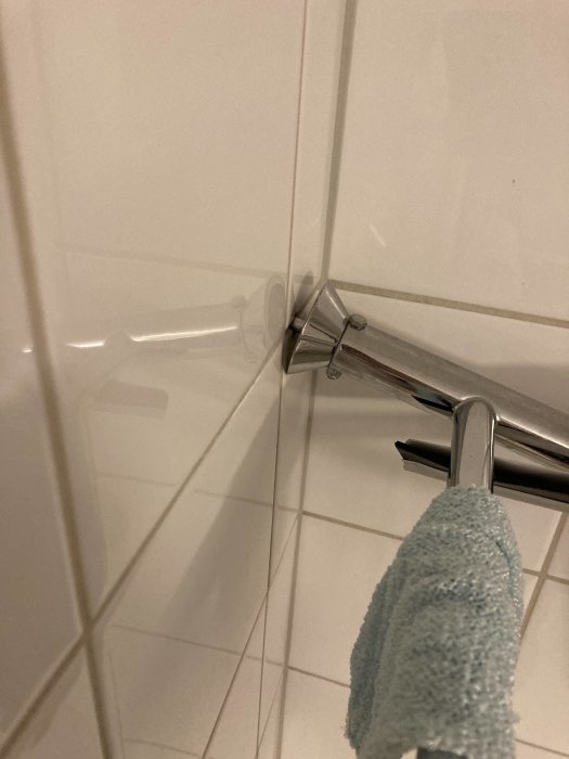 Hörn av ett badrum, kakelväggar, handdukshängare med ljusgrön handduk.