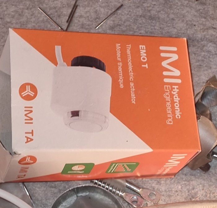 En produktförpackning för en termoelektrisk ställdon från IMI Hydronic Engineering, omgiven av några verktyg.