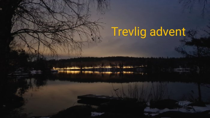 Kvällsutsikt över en sjö med ljus, snöfläckar, trädgrenar och texten "Trevlig advent".