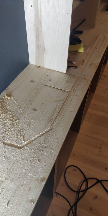 Träsågspån på golv, kabel, vit plywood, oavslutat snickeriarbete eller renovering inomhus.