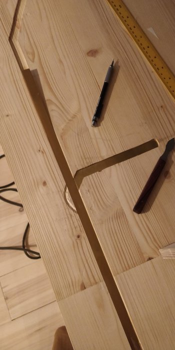 Trägolv, metallinjal, penna, kniv; verktyg och material för hantverk eller snickeri.