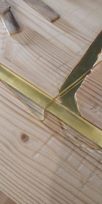 En närbild av träplankor och gula metallprofiler, möjligen en del av en möbel eller konstruktion.