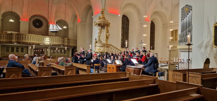 Kör framträder i kyrka, publik ser på, orgeln, klassisk arkitektur, ljuskronor, rofylld atmosfär.