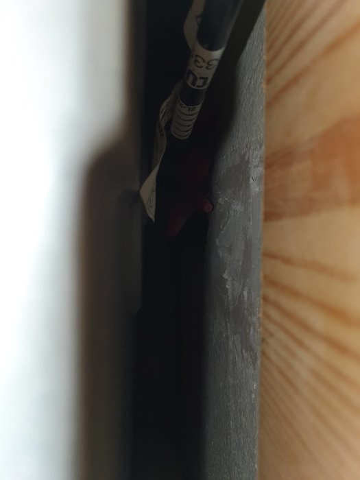 Mörkt utrymme, ser dagstidning, trådklump, trångt mellanrum mellan vägg och möbel eller konstruktion.