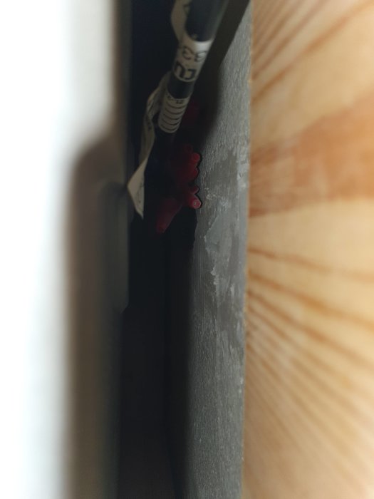 Mörk glipa med kantade föremål, kabel och trähörn; otydligt med skymd sikt.