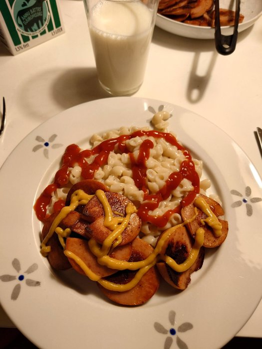 Ett fat med pasta, korv, ketchup och senap med mjölk och bacon i bakgrunden.