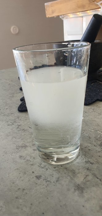 Ett glas med grumlig vätska, kanske vatten, på en bänkskiva med en svamp bakom.