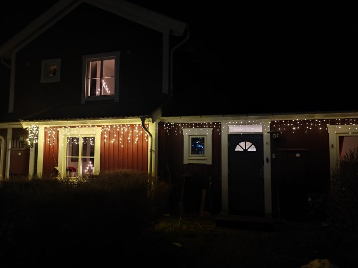 Ett mörkt hus dekorerat med ljusslingor på kvällen.