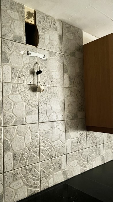 Vägg med stenmönstrade kakelplattor, delvis oavslutad renovering, utstickande elinstallation, träpanel, öppet utrymme i taket.