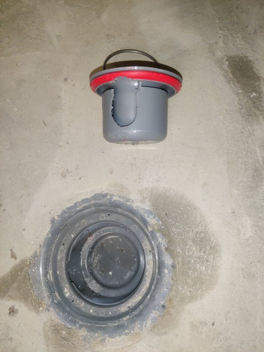 Hink hängande ovanför öppen bottenventil på en betongyta, vatten droppar, konstruktion, gråa och röda toner.