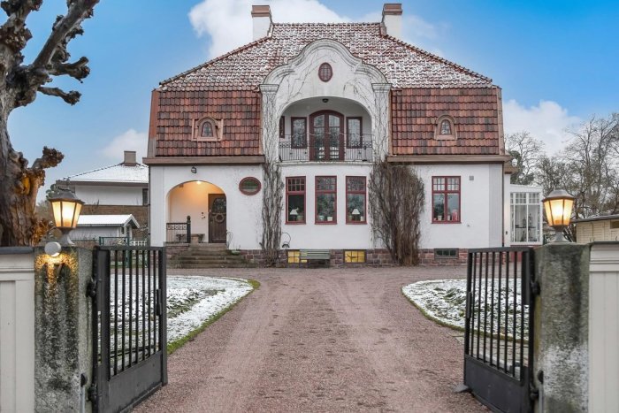 Vit klassisk villa, tegeltak, öppet svart staket, infart, snöfläckar, tidig vinter eller sen höst.