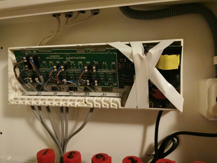 Elektronisk kretskort i låda med kablar och tejp, delvis täckt, installationsarbete eller reparation pågår.