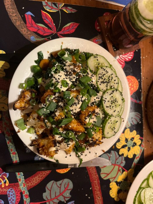 En tallrik med mat, bestående av grönsaker och quinoa, och en dryck med gurkskivor på ett livligt duk.