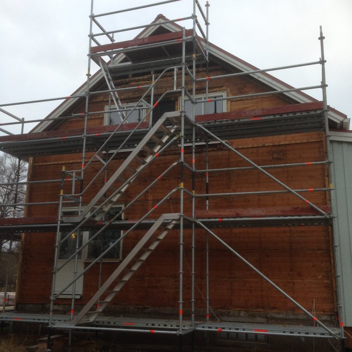 Ett hus med röd träfasad täckt av byggställningar under renovering eller byggarbete.