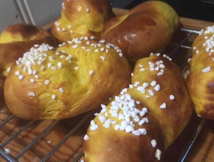 Nybakade saffransbullar med pärlsocker på ett galler. Ljusa, flätade och ser goda ut.