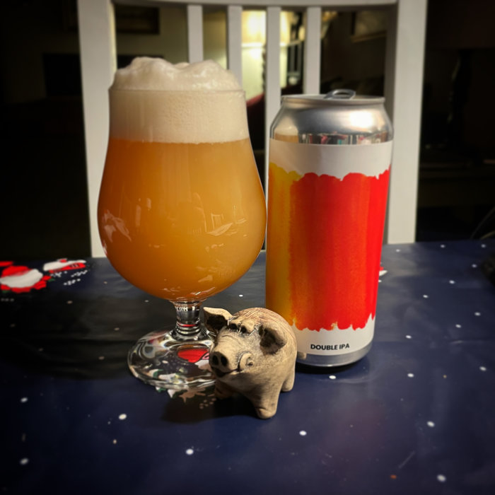 Ölglas med skum, burk Double IPA, liten trägris, bordduk med stjärnor.