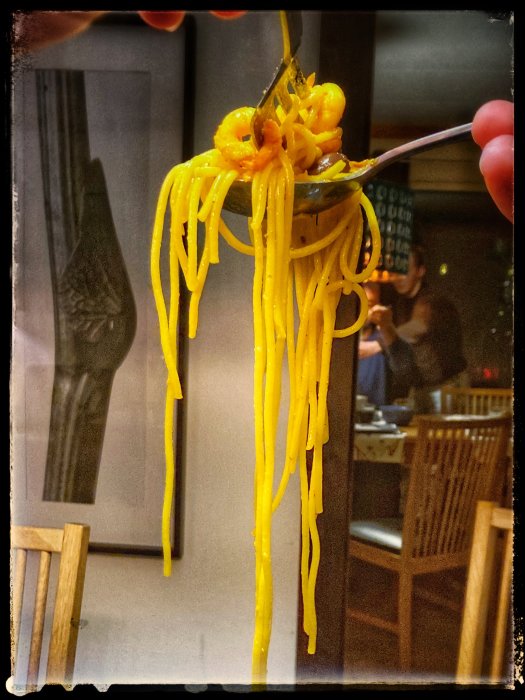 Gaffel håller upp spagetti med kryddor, i en restaurangmiljö.