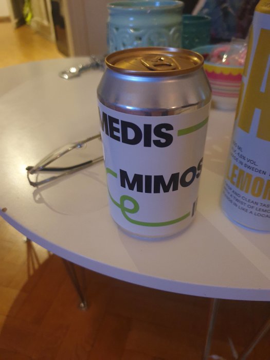 En burk på ett bord nära glasögon, suddig bakgrund. Text på burken: "MEDIS MIMOSA".
