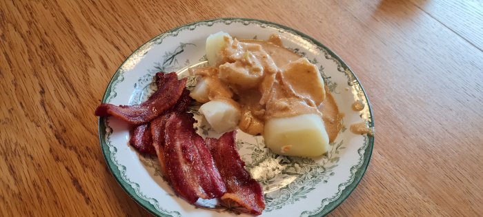 Tallrik med bacon, potatis och brunsås, traditionell maträtt, enkelt upplagt, trämönstrat bord.