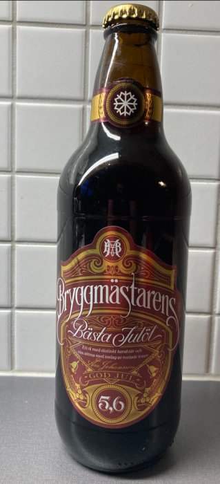 Brun glasflaska med etikett, "Bryggmästarens Bästa Julöl", julöl, 5,6 % alkohol, kök kakelbakgrund.