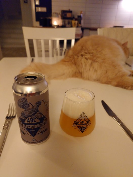 Ett ölglas, burk, bestick och en röd katt på ett vitt bord.