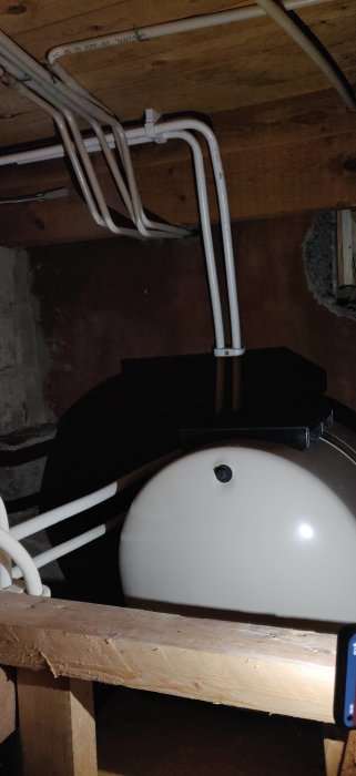 Mörk utrymme, elektriska ledningar, träbjälkar, stora vit objekt, smartphone synlig nere till höger.