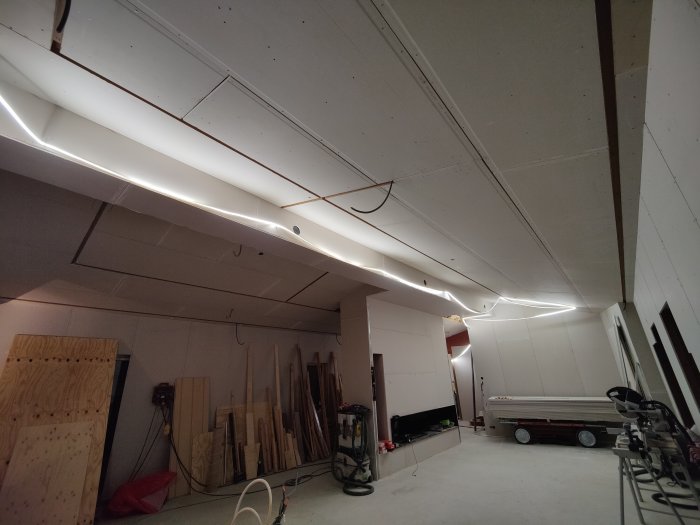 Verkstadslokal under renovering med längsgående LED-belysning, trämaterial, och en parkerad båt.
