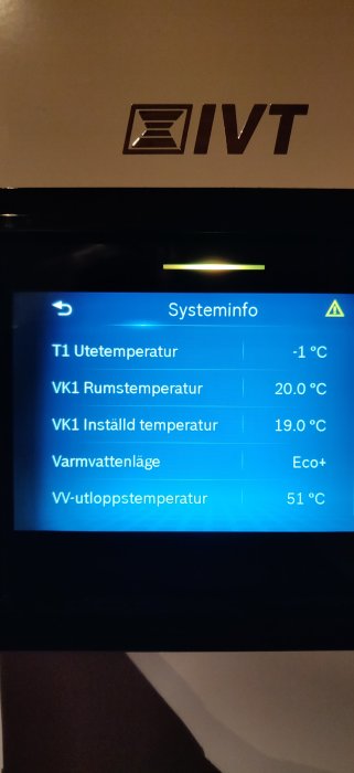 Digital display visar temperaturinformation och inställningar för värmesystem, inne i ett mörkt rum.