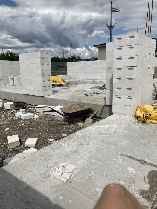 Byggarbetsplats under konstruktion med tegelväggar, betonggolv, byggmaterial och molnig himmel i bakgrunden.