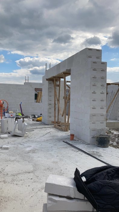 Byggarbetsplats med vita murblock under konstruktion, byggmaterial spridda, delvis molnig himmel.