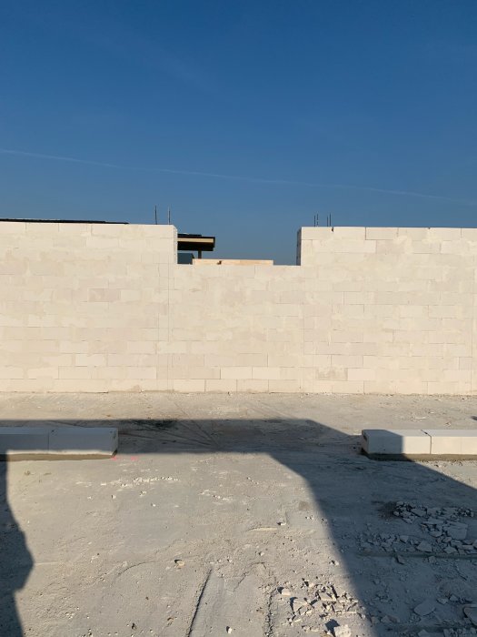 Nybyggnad av betongblock, under konstruktion, mot en klarblå himmel. Skuggor syns på marken.