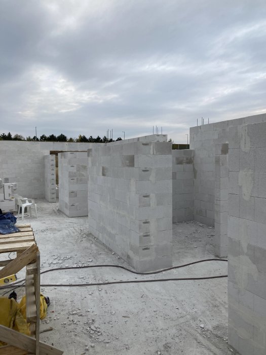 Byggarbetsplats, grå betongblocksväggar under konstruktion, armeringsjärn sticker upp, byggmaterial, molnig himmel bakgrund.