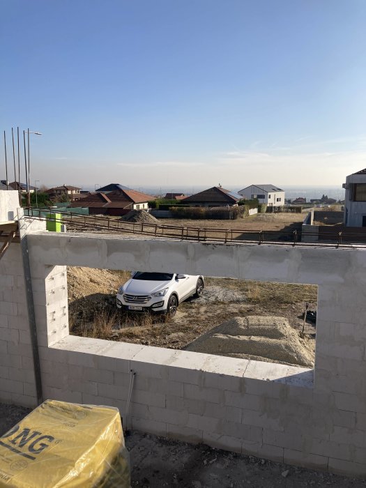 En byggarbetsplats med en bil synlig genom en öppning i en mur med hus och klar himmel i bakgrunden.