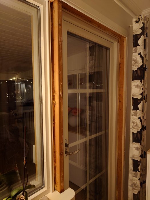 Fönsterdörr med vit handtag, träramar, reflektion, gardiner, kvällsbelysning inomhus.