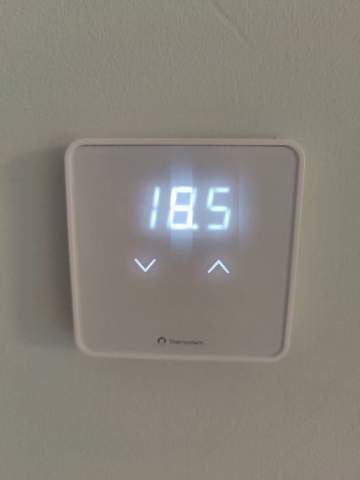 Digital termostat visar inomhustemperatur 18.5 grader Celsius på en vägg.