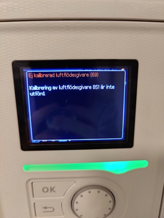 Elektronisk apparat med skärm visar felmeddelande om okalibrerad luftflödesgivare, omgiven av plast och knappar.