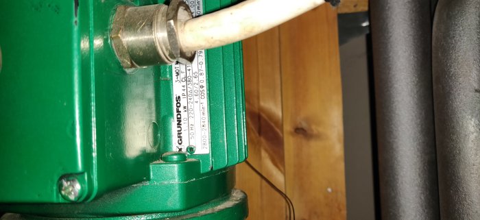 Grundfos cirkulationspump, teknisk specifikationsetikett, anslutna rör, träbakgrund.