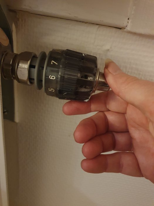 En hand justerar termostat på radiator, siffror synliga, vit bakgrund, interiör, värmeinställning, hushåll, energianvändning.