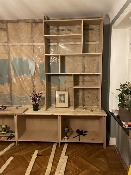 Orenoverat rum med halvfärdig hylla, verktyg, träplankor och isolering på väggen.