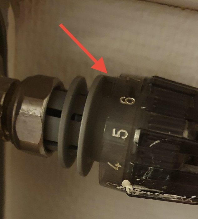 Närbild av termostatventil på radiator, röd pil pekar på justeringsmekanism.