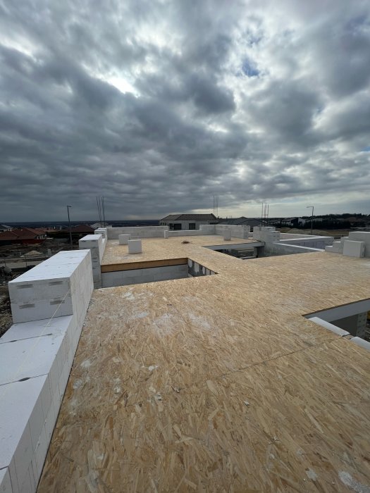 Byggarbetsplats med oslipade träplattor och vit isolerblocksstruktur under en dramatisk molnhimmel.