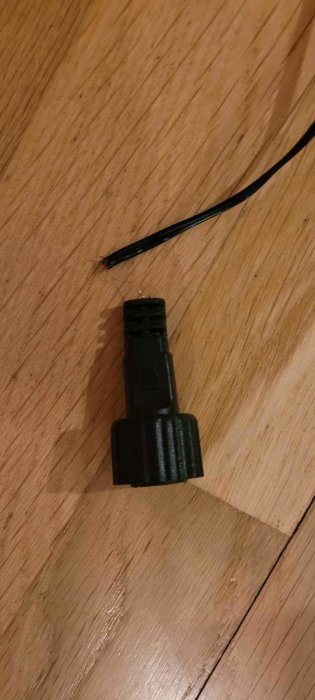 Trasig svart HDMI-adapter med exponerade ledningar på trägolv.